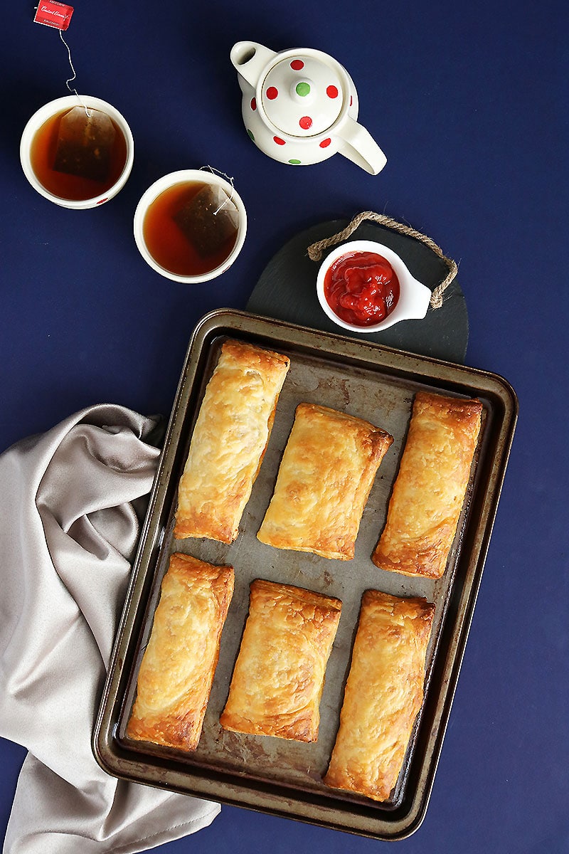 Freshly baked Maruti Live Puff pastries on a baking tray served with tea and tomato ketchup